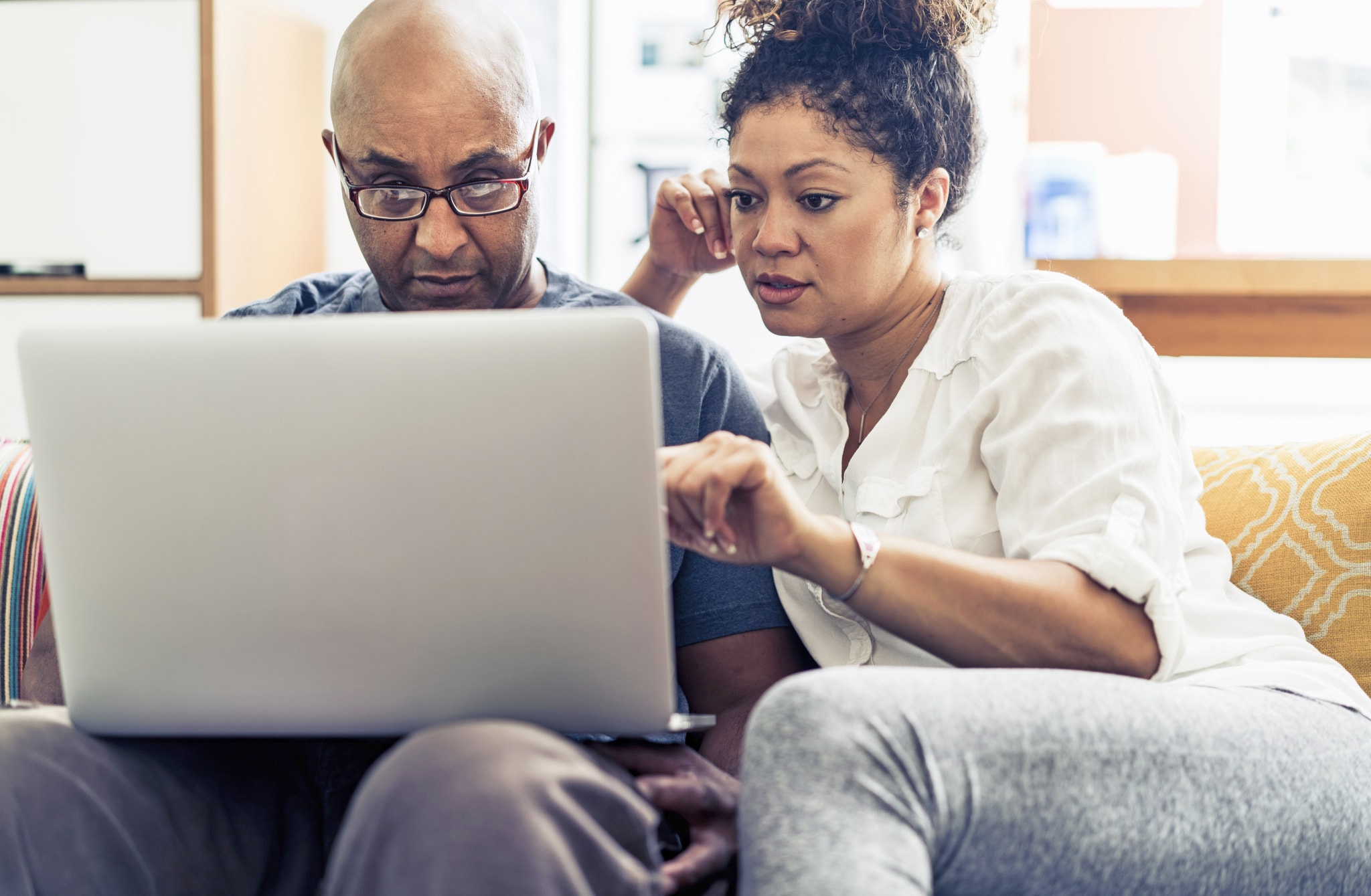 A man and a woman sitting on a couch looking at a laptop