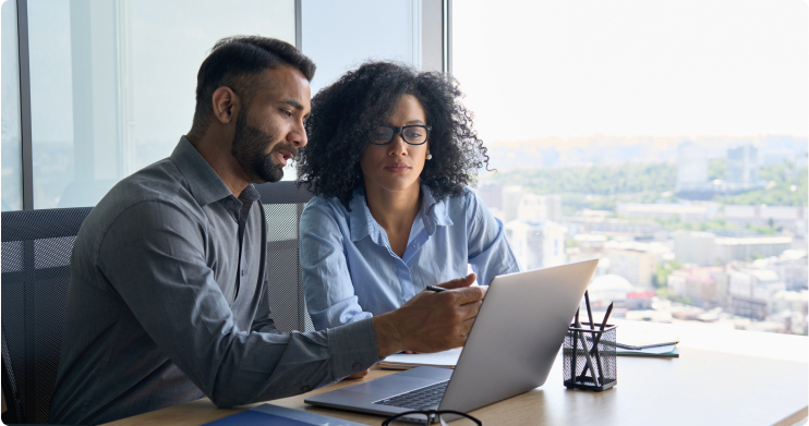 Two coworkers sitting in front of a laptop discussing.