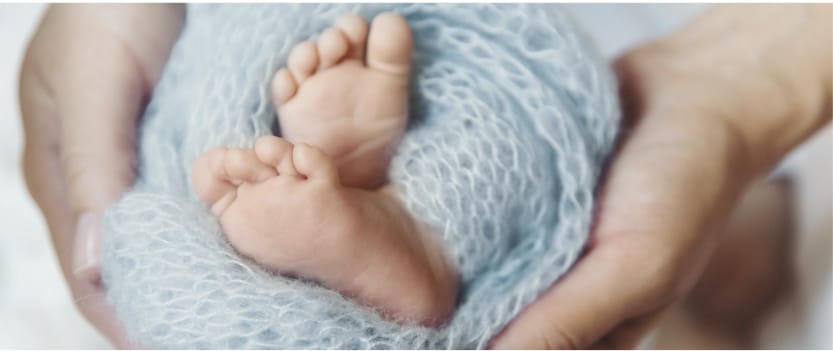 Image of baby feet rolled in a blue knitted blanket with two hands holding the sides of the baby