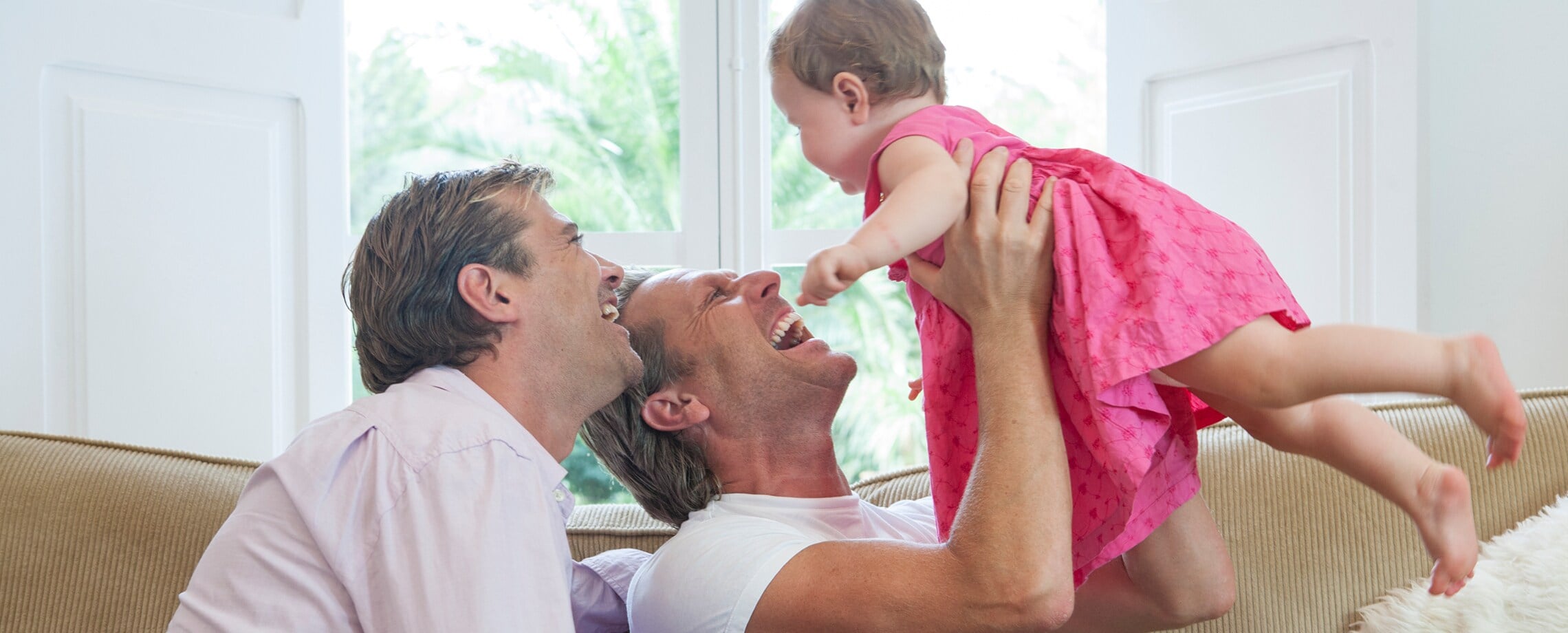 Two males laughing with baby wearing pink dress