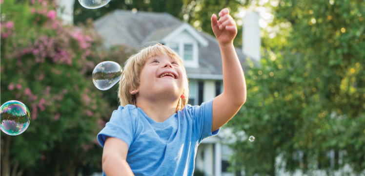 Young boy, with special needs, smiling at bubbles outside