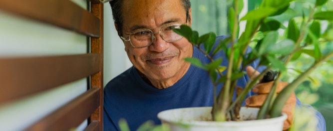 A man wearing a blue shirt and glasses, smiling, while looking at a plant