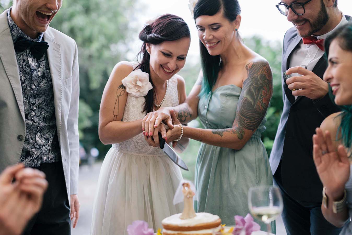 Two women in wedding dresses smiling cutting a wedding cake together