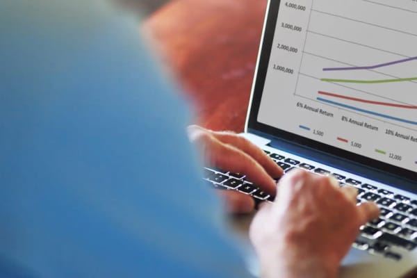 Hands typing on a laptop and the laptop shows a line chart