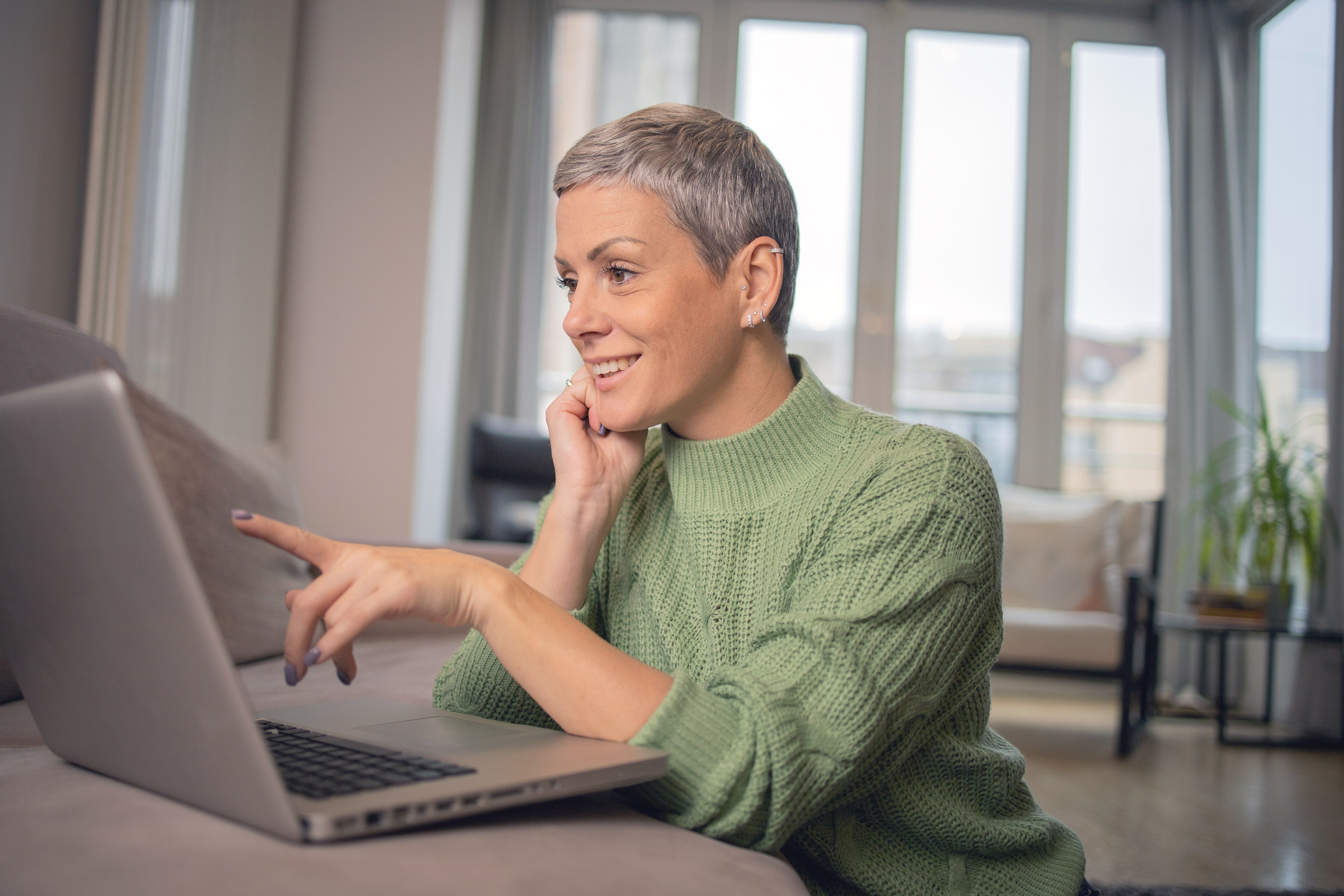 woman in green knitted sweater pointing at laptop smiling