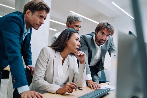 four office workers inspect work on a computer screen together