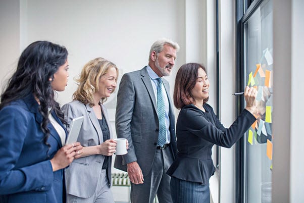 team of four employees using stick notes on window to collaborate