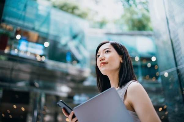 woman with short black hair holding a cellphone and folder smiling