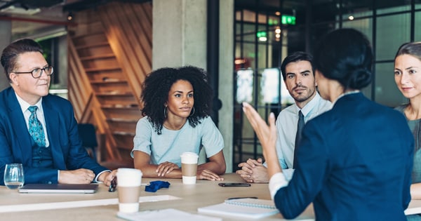 A group of workers sitting around a table listening to another coworker speak